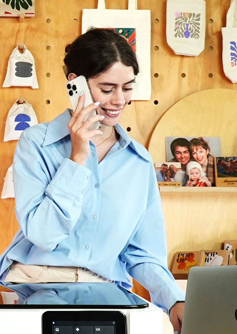 Nasmejana preduzetnica telefonira, u pozadini primeri FLUX Ador radova.